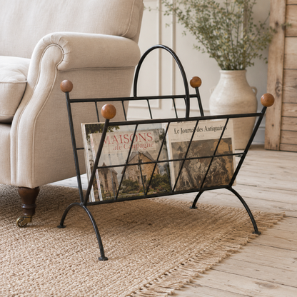 Wrought iron magazine rack with books on a wooden floor in a living room setting.
