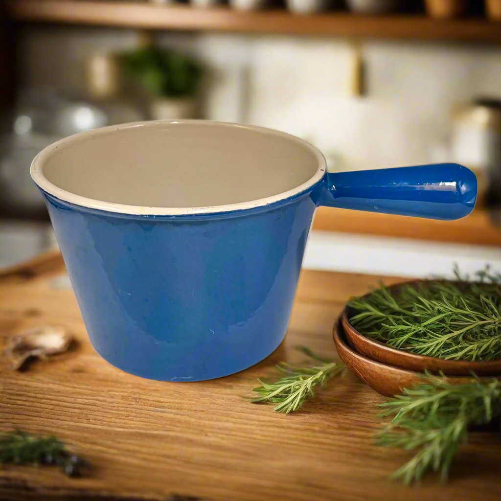 Blue cast iron ceramic pot with beige interior on a wooden surface, surrounded by greenery.