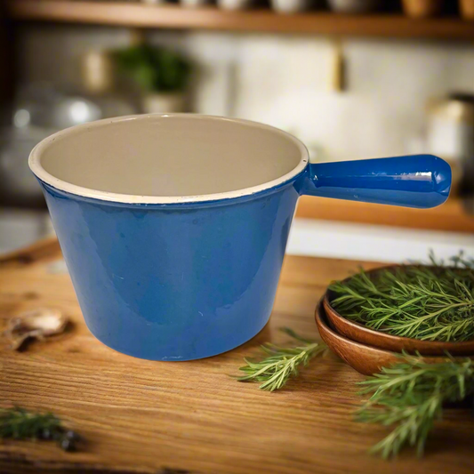 Blue cast iron ceramic pot with beige interior on a wooden surface, surrounded by greenery.
