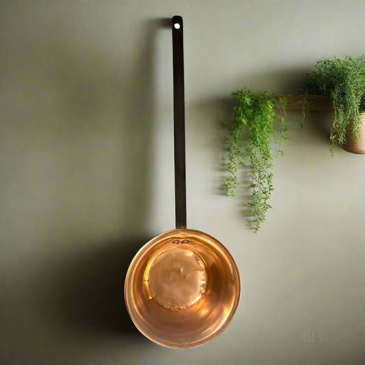 copper ladle pan with a black handle on a green background