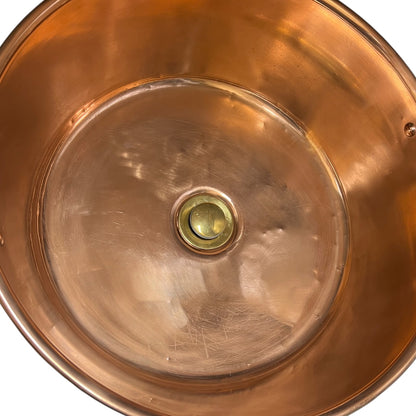 Close-up of the interior of a copper sink basin with a polished brass drain cover, showing the metallic copper walls and reflective surface against a white background.