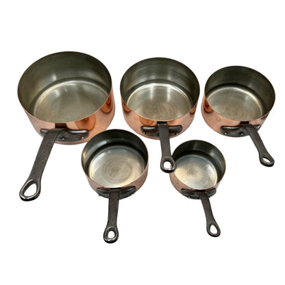 Five copper and tin lined saucepans of varying sizes with dark metal handles, arranged on a plain white background.