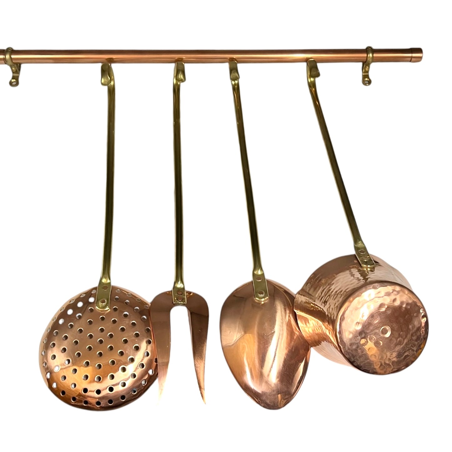 A set of hanging copper kitchen utensils on a brass rod, including a perforated skimmer, a spatula, a turner, and a small hammered pot, shown against a plain white background.