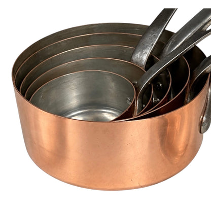 A set of nested copper and stainless steel measuring pots with handles, shown on a plain white background.