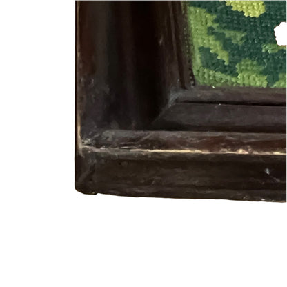 Close-up detail of a dark brown wooden frame corner with a green and yellow needlepoint canvas visible inside, shown against a white background.