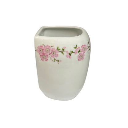 A white ceramic planter pot with a pink cherry blossom floral pattern around the middle, set against a plain white background.