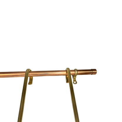 A close-up of a copper rod with gold-toned metal brackets and hanging rings, shown against a plain white background.