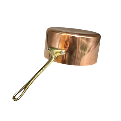 A copper saucepan with a shiny metallic finish and a long, textured brass-colored handle, shown on a plain white background.