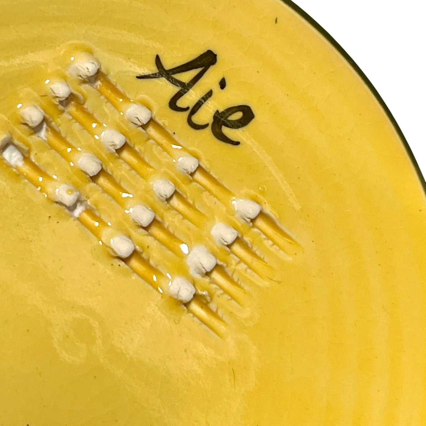 A yellow plate featuring a green pepper and the French word for garlic, “Ail,” designed for grating garlic and perfect for a French farmhouse-style kitchen, set against a white background.