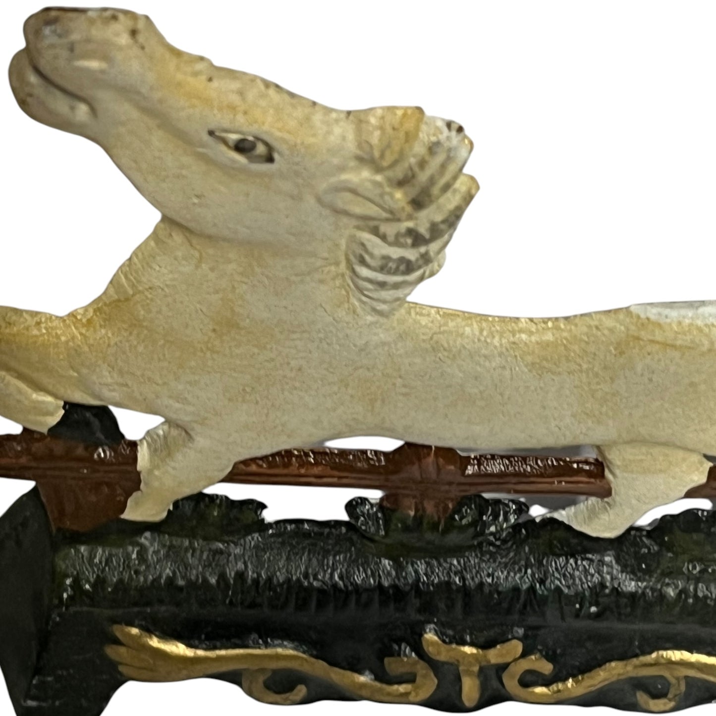 A close-up of a decorative horse figurine or sculpture in a light cream color, mounted on a dark brown and black base with gold accents, against a plain white background.