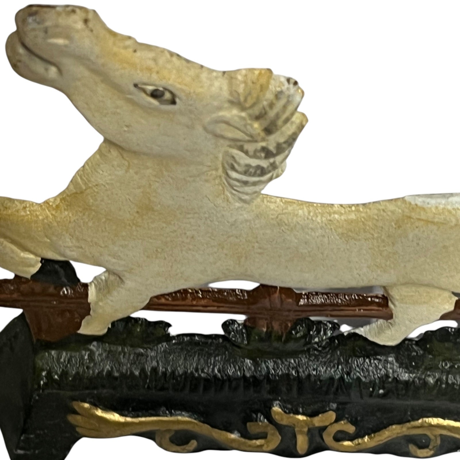 A close-up of a decorative horse figurine or sculpture in a light cream color, mounted on a dark brown and black base with gold accents, against a plain white background.