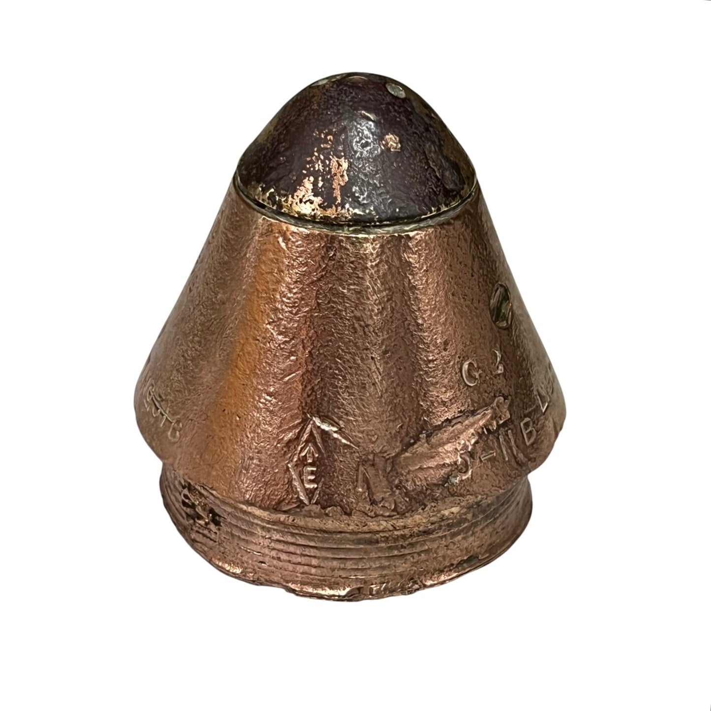 A vintage copper-colored metal capsule or container with a conical top and embossed markings, shown against a plain white background.