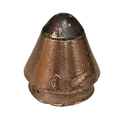 A vintage copper-colored metal capsule or container with a conical top and embossed markings, shown against a plain white background.