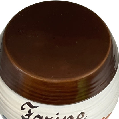 Close-up of a ceramic jar lid with a glossy dark brown glaze and part of a white body visible, on a plain white background.