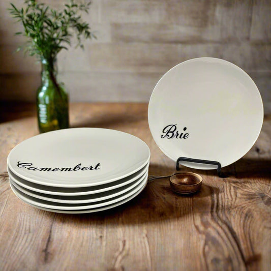 Set of ceramic cheese dishes with 'Camembert' and 'Brie' labels with a rustic kitchen in the background