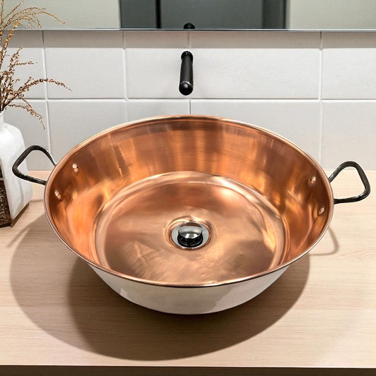 Copper sink with handles on a wooden surface with a tiled wall background