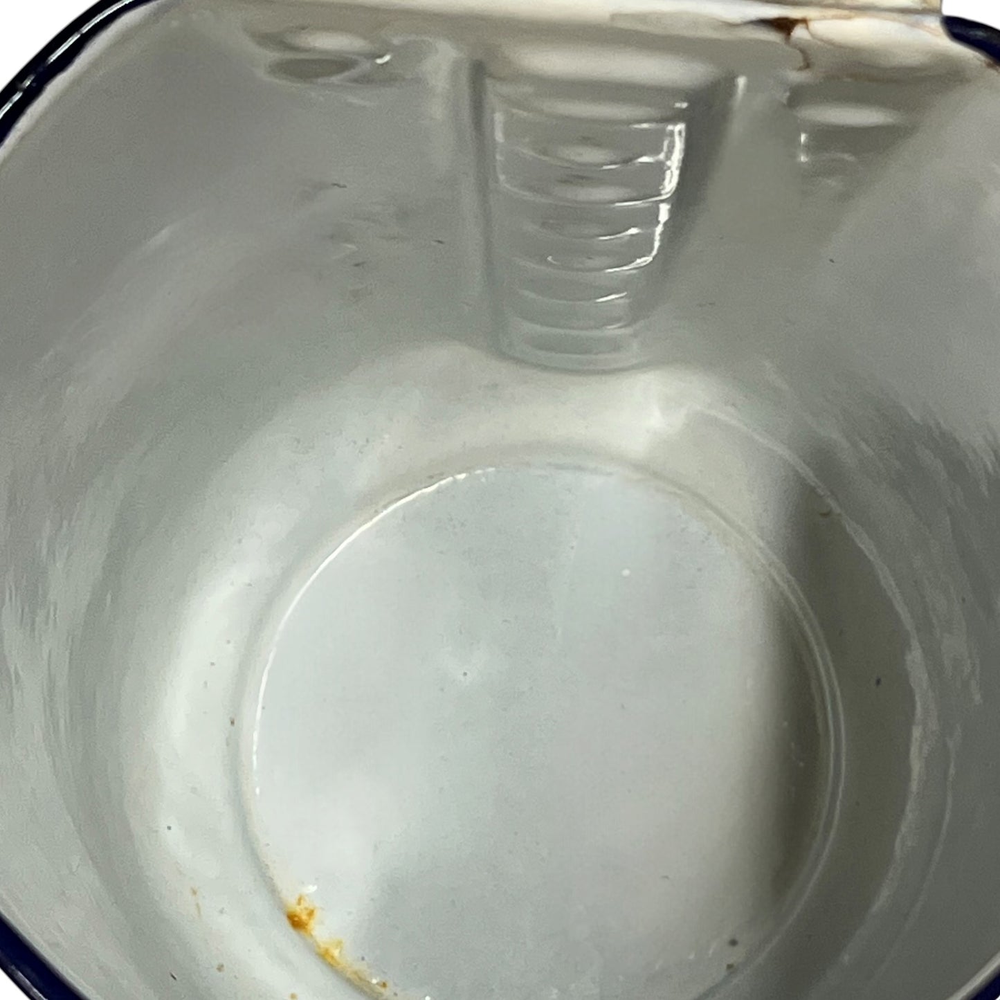 An empty white enamel pitcher pot viewed from above, showing the interior, ribbed rim, and a small amount of residue near the bottom.