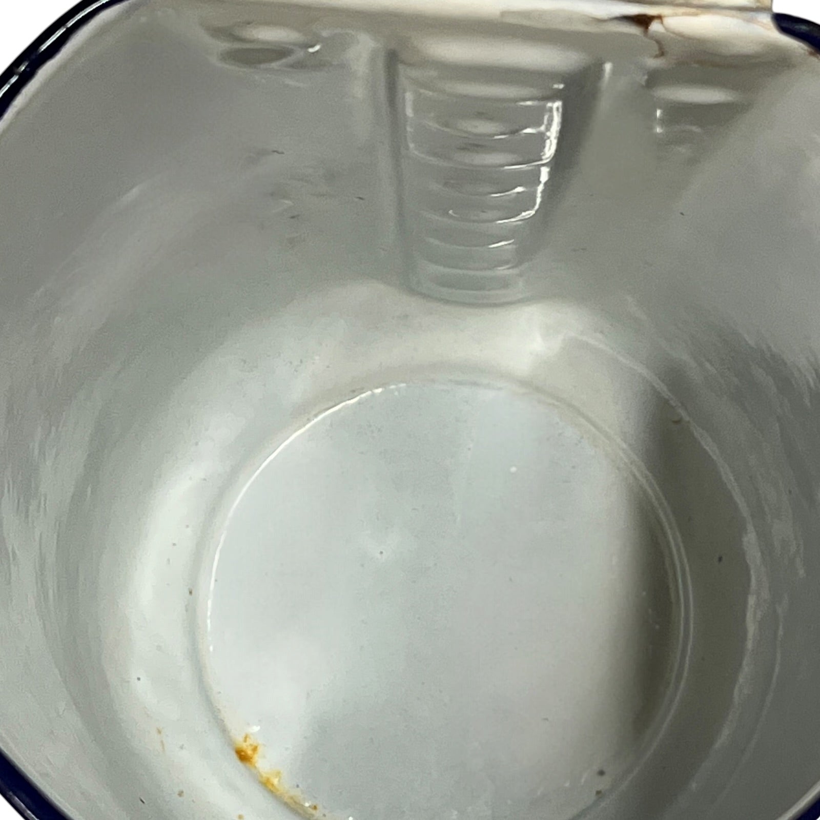 An empty white enamel pitcher pot viewed from above, showing the interior, ribbed rim, and a small amount of residue near the bottom.
