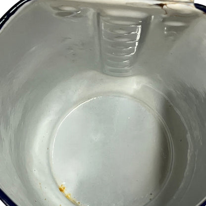An empty white enamel pitcher pot viewed from above, showing the interior, ribbed rim, and a small amount of residue near the bottom.