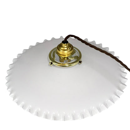 A white glass ceiling light fixture with a scalloped edge and a brass central socket, connected to a dark brown cord, shown against a plain white background.