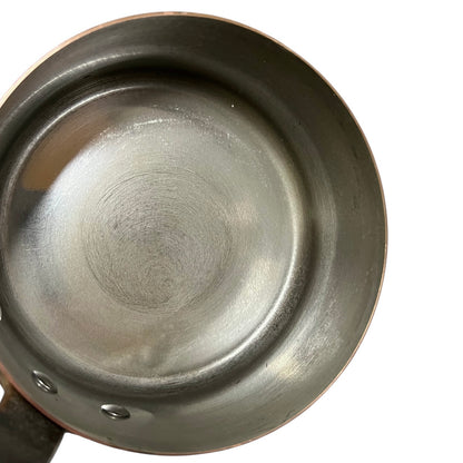 Top-down view of a copper tin lined saucepan or small pot showing the interior surface and part of the rim against a white background.