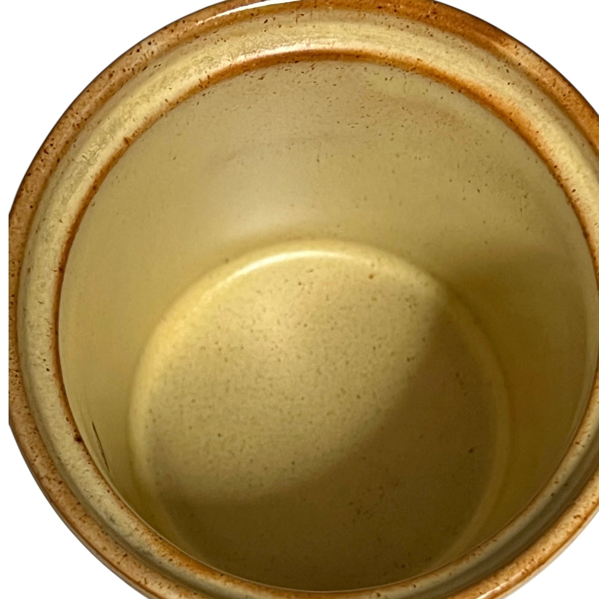 Close-up top-down view of a ceramic pot or crock with a warm beige interior and a brown speckled rim on a white background.