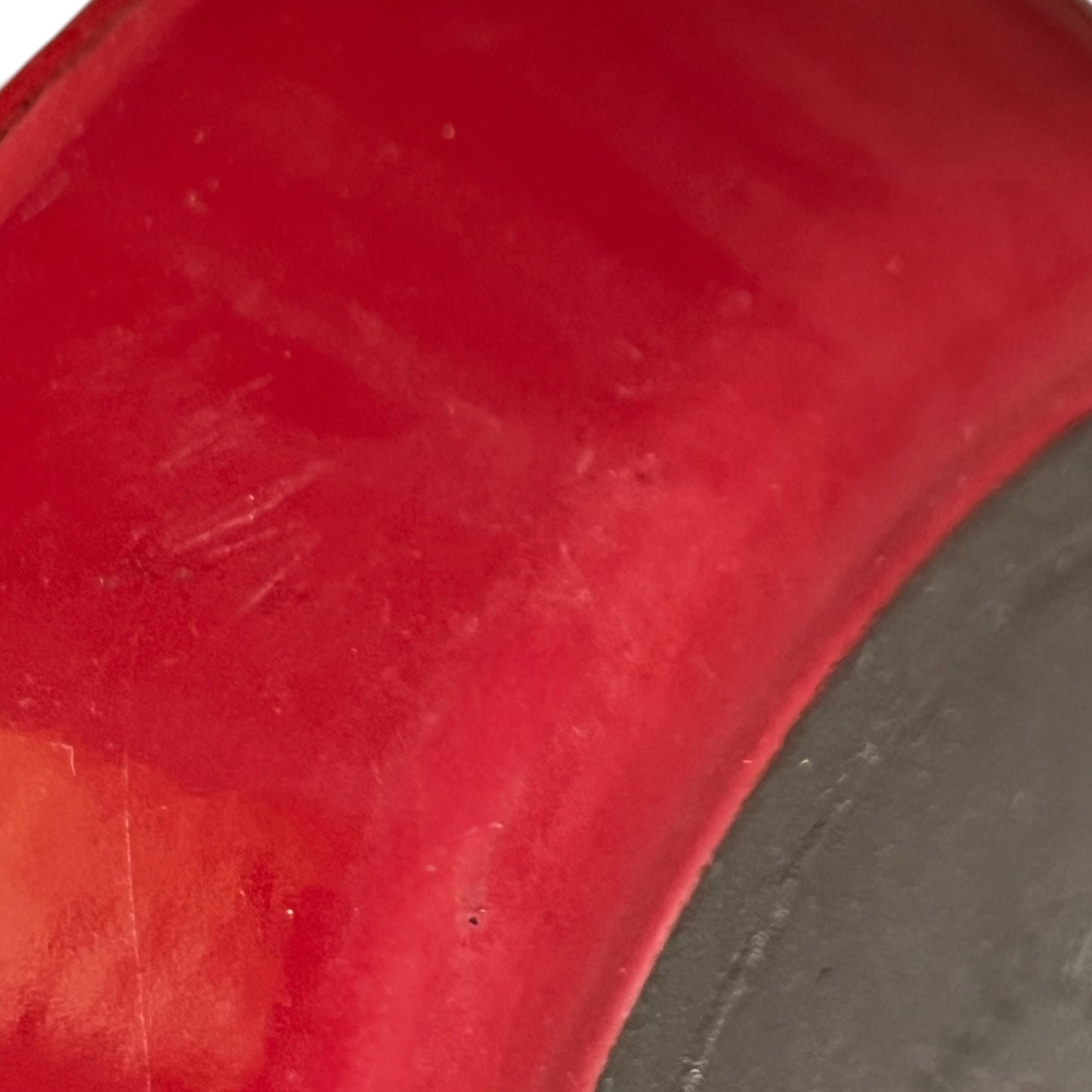 A close-up of a red cast iron cousances Le Creuset dish and scratches on the red material and a dark gray side edge.