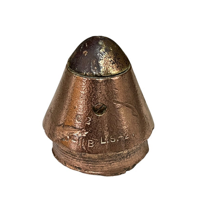 A solid brass fuse with a conical shape, featuring engraved markings and a dark oxidized top surface, shown on a plain white background