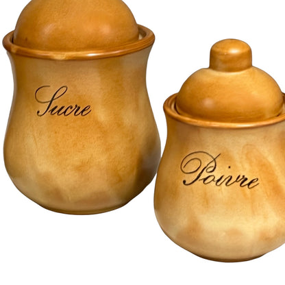 Two glazed ceramic canisters with lids, one labeled 'Sucre' and the other 'Poivre' in black cursive script, set against a plain white background.