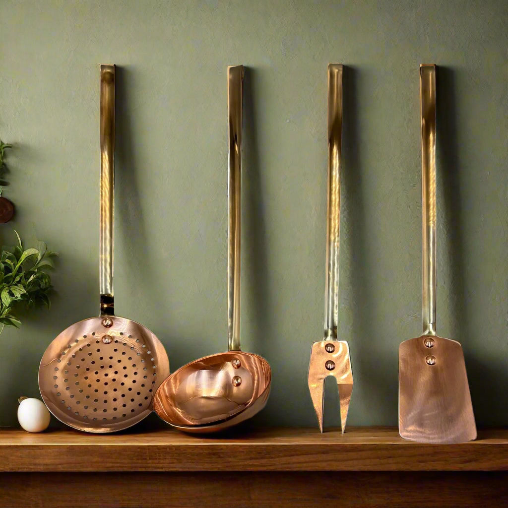 Set of 4 French copper and brass utensils including a slotted spoon, ladle, fork and spatula on a wooden counter top