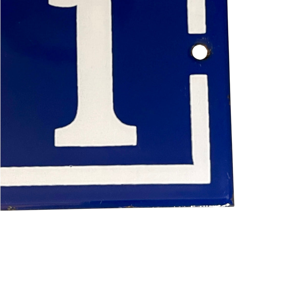 A close-up of a blue square sign or plaque with a large white letter 'I' and white border lines, plus a small circular hole near the top right, shown against a white background.