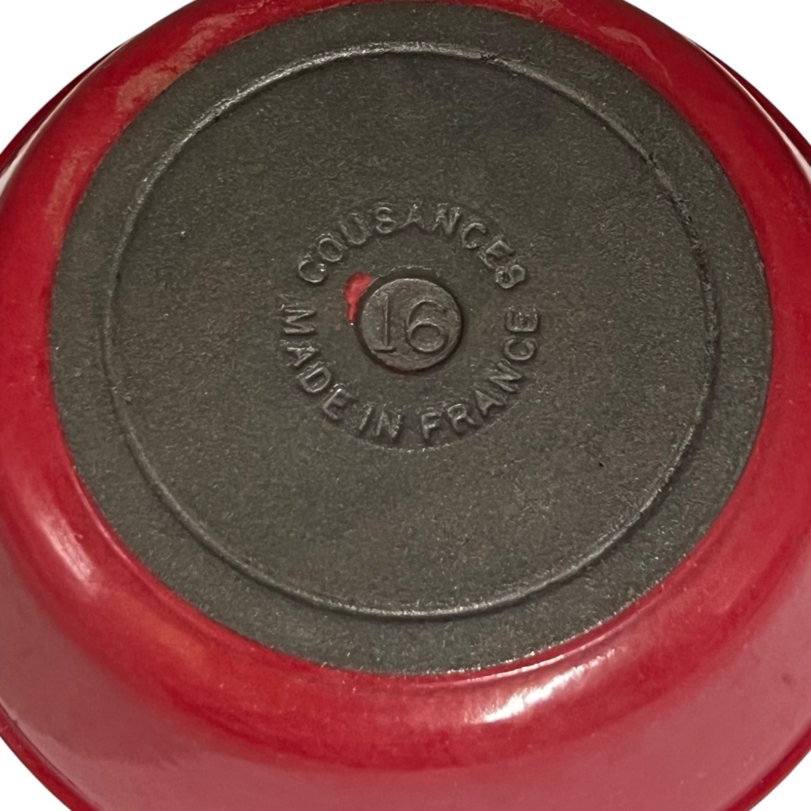 Close-up of the bottom of a red enameled cast iron pot or pan, showing a dark gray non-stick coating and embossed text that reads 'COUSANCES MADE IN FRANCE' with a size '16' logo in the center.