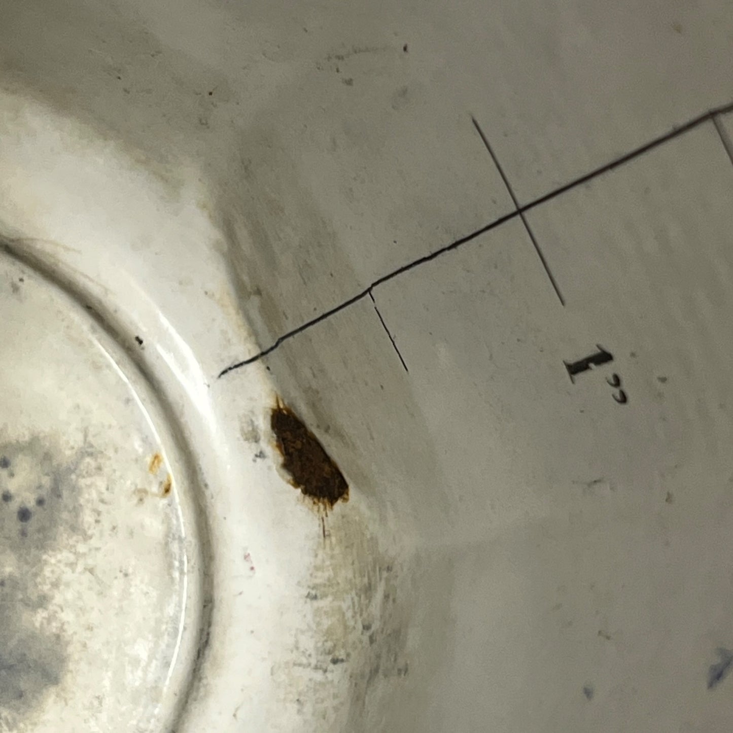 Close-up of the inside of a white enamel pot showing a small brown stain near a printed measurement line and number 1 1/2.