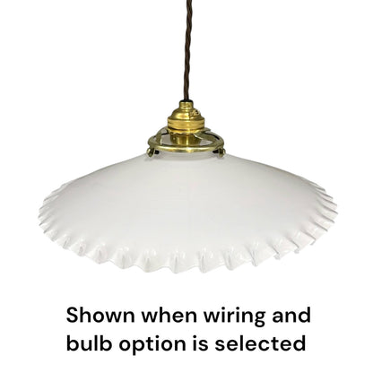 A white glass pendant light with a flared, scalloped rim and a brass-colored metal fixture, suspended by a dark cord. Text at the bottom reads, 'Shown when wiring and bulb option is selected'.