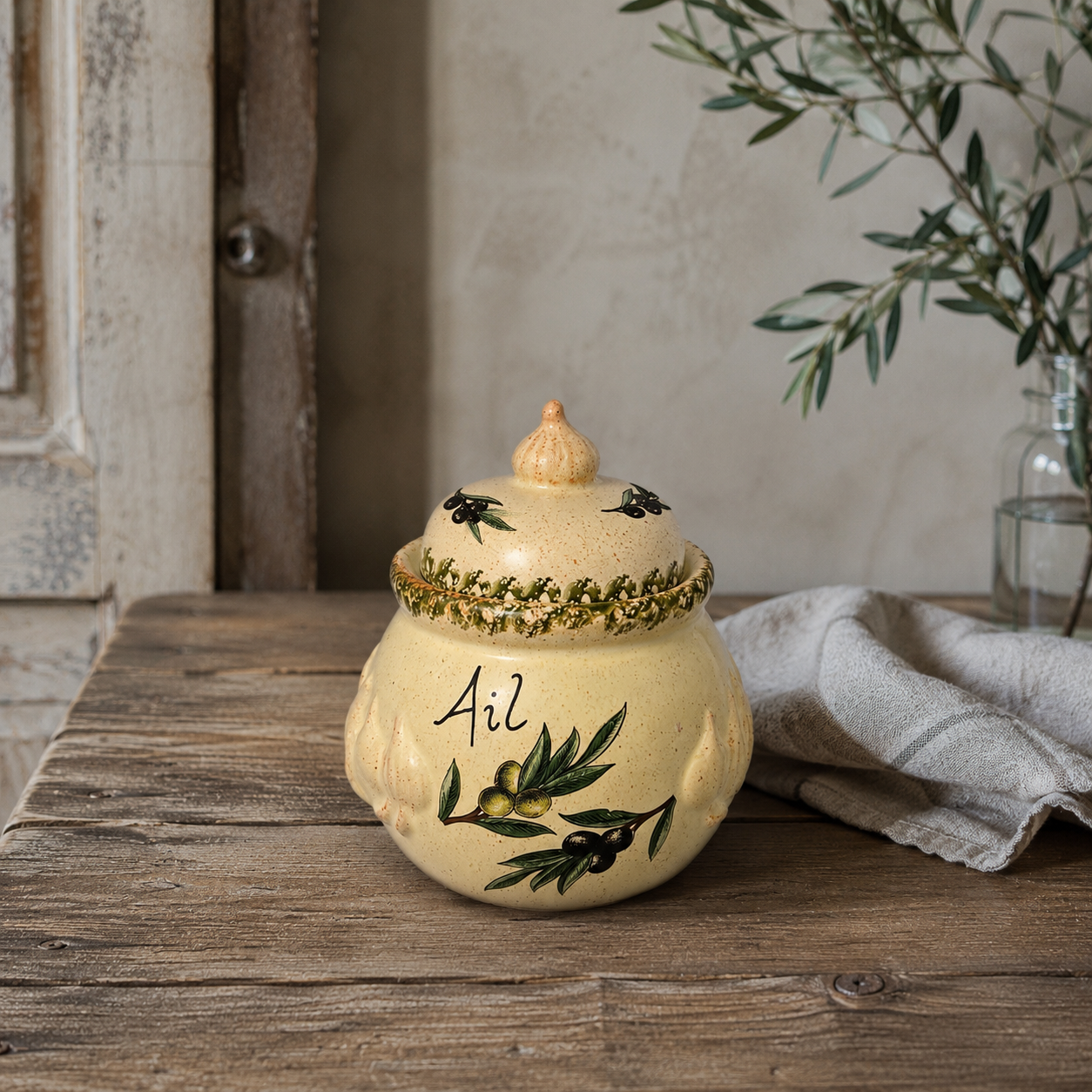 Decorative ceramic jar with lid on a wooden surface, featuring olive designs and the word 'Ail', ideal for a farmhouse kitchen 