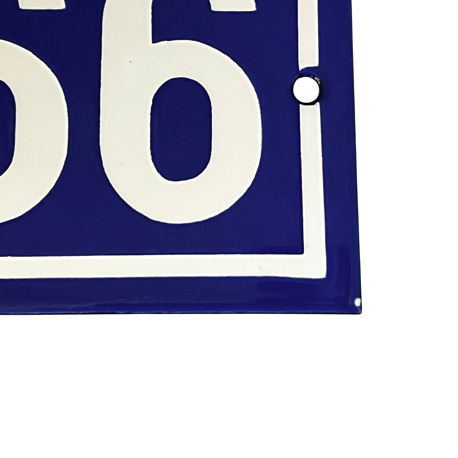 Close-up of a blue and white enamel-style sign showing part of a large white numeral on a dark blue background, with a small metal grommet visible on the right edge.