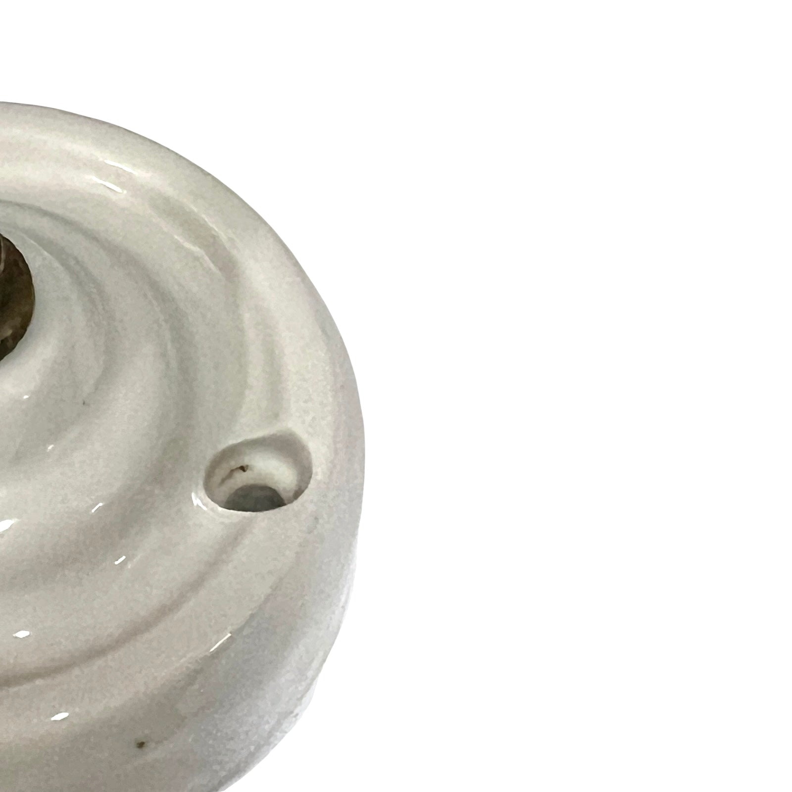 A close-up of a glossy off-white ceramic or porcelain object with a circular ridged surface and a small hole, cropped on the left side against a plain white background.
