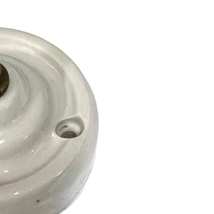 A close-up of a glossy off-white ceramic or porcelain object with a circular ridged surface and a small hole, cropped on the left side against a plain white background.