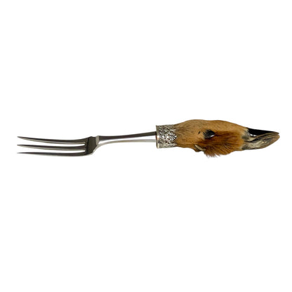 A vintage-style metal serving fork with a decorative handle shaped like a small animal skull, featuring brown fur, a black eye, and silver-toned metal details, shown against a plain white background.