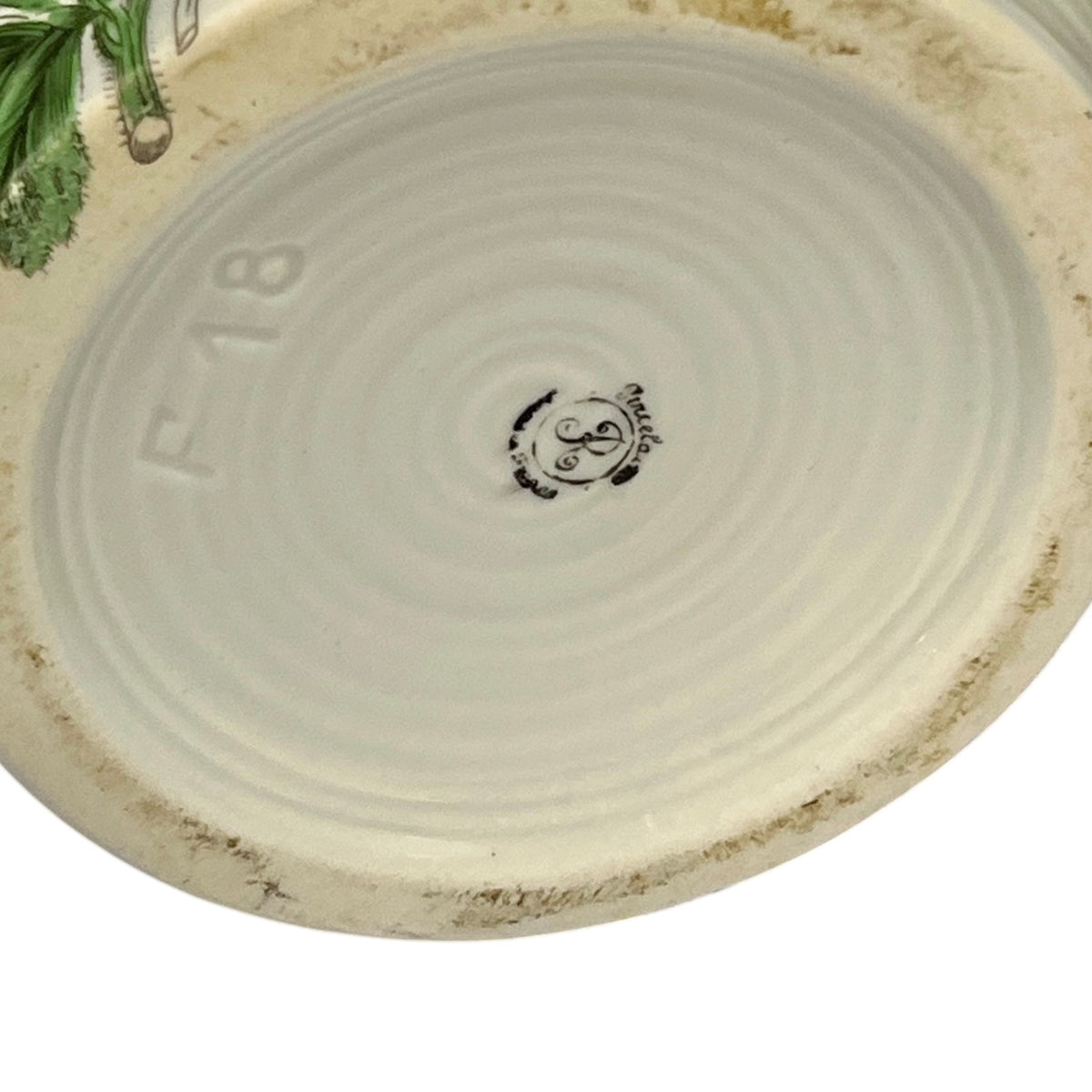 Close-up of the bottom of a round ceramic pot, showing a light beige glazed interior with concentric ring texture, embossed 'F18' text, a small central maker's mark, and a rougher unglazed rim.
