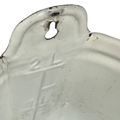 A close-up of a white measuring container with embossed measurement markings and a keyhole-shaped hole near the rim, showing some wear and dirt on a white background.