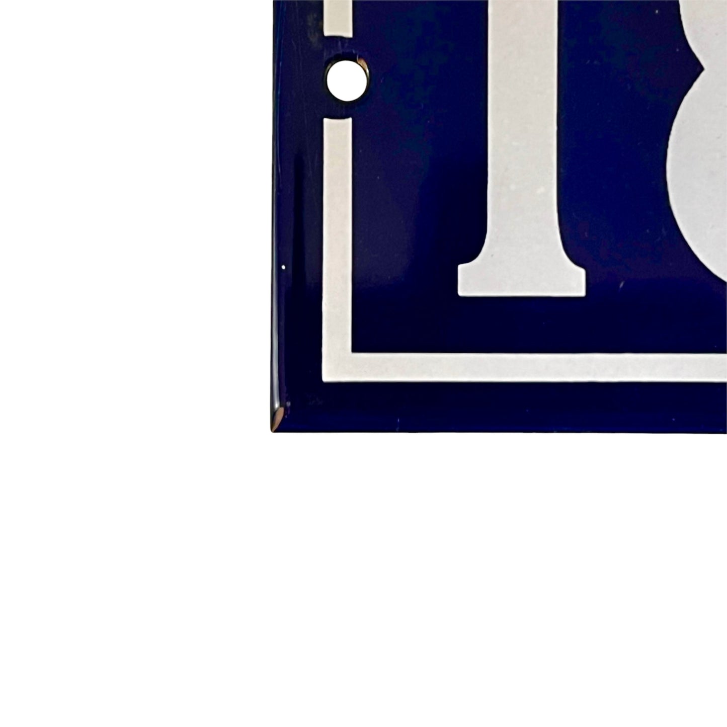 Close-up of a dark blue and white house number plaque, showing the corner with a mounting hole on a plain white background.