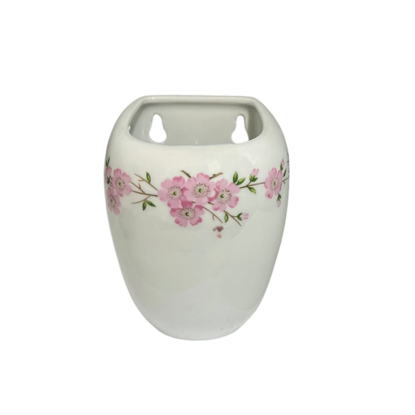 A white ceramic toothbrush pot with a pink cherry blossom floral pattern around the middle, featuring two cutout holes at the top for plant stems, set against a plain white background.