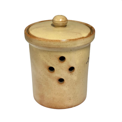 A handmade ceramic storage jar with a matching lid, featuring a speckled beige and cream glaze with a rustic brown rim and four ventilation holes on the side.