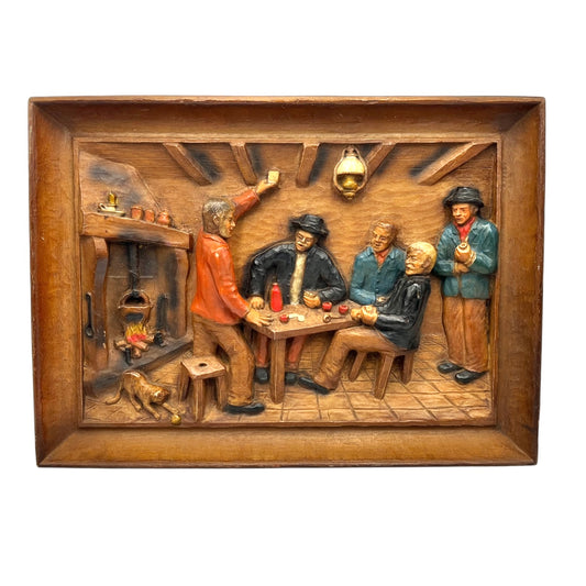 Wooden relief picture of a group of people around a table in a rustic setting on a white background.