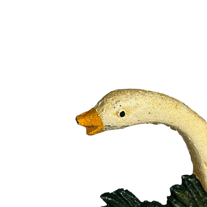 Close-up of a goose figurine head with a textured cream body, orange beak, and dark green base on a plain white background.