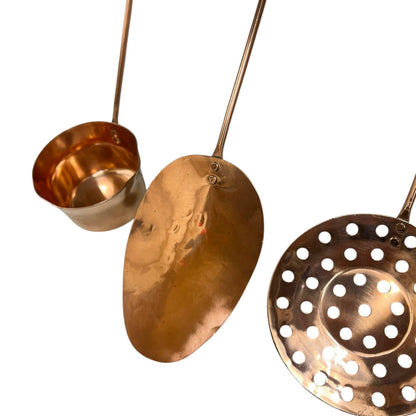 Close up of 3 copper utensils on a copper hanging bar on a white background