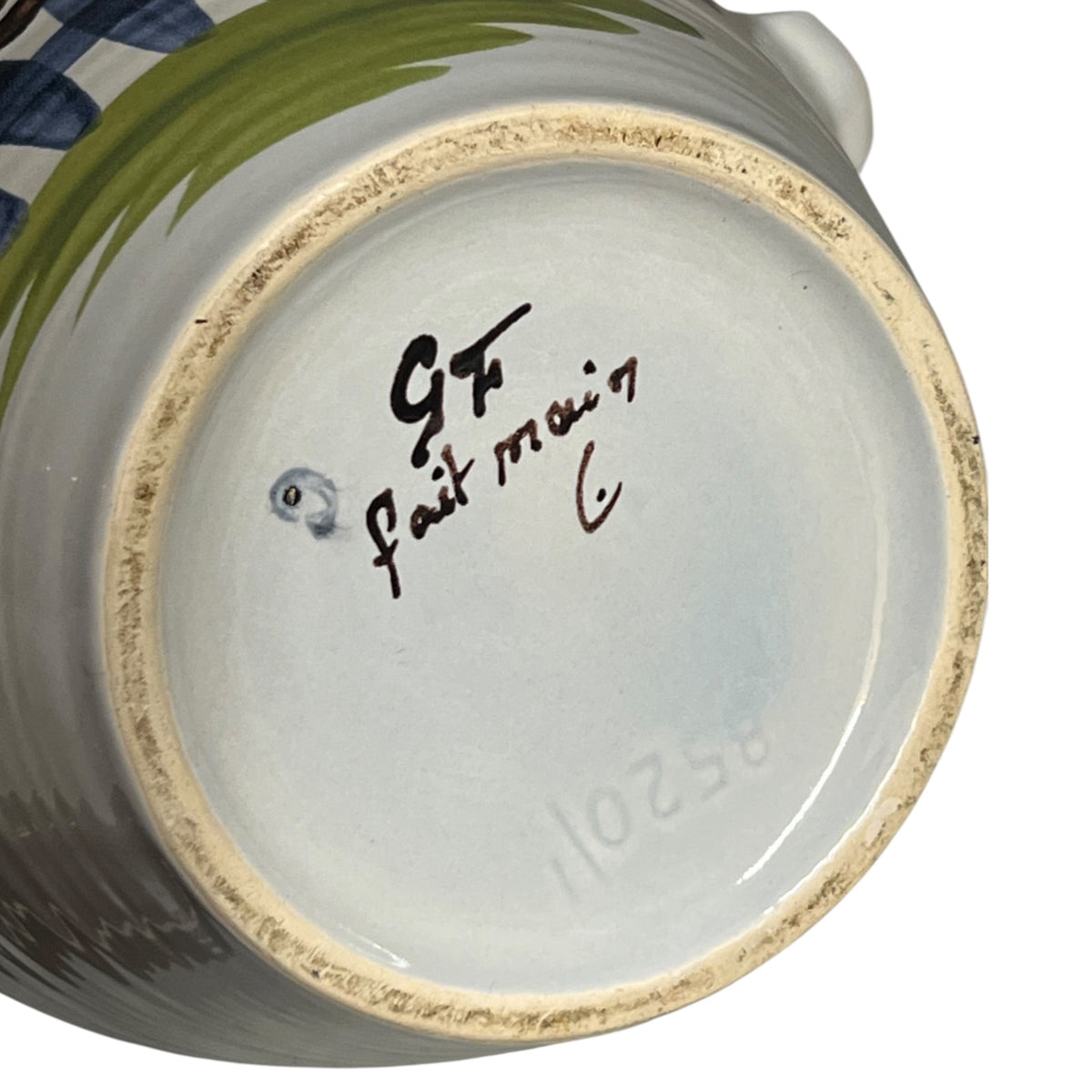 Close-up of the bottom interior of a ceramic vessel, showing a light blue glazed base with a hand-painted signature reading '9GF Fait main ' and a small blue dot, plus a beige unglazed rim.
