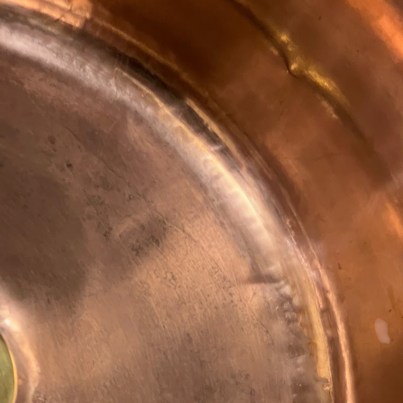 Close-up of the interior of a copper or bronze pot, showing the metallic surface and rim with a warm coppery-brown finish.