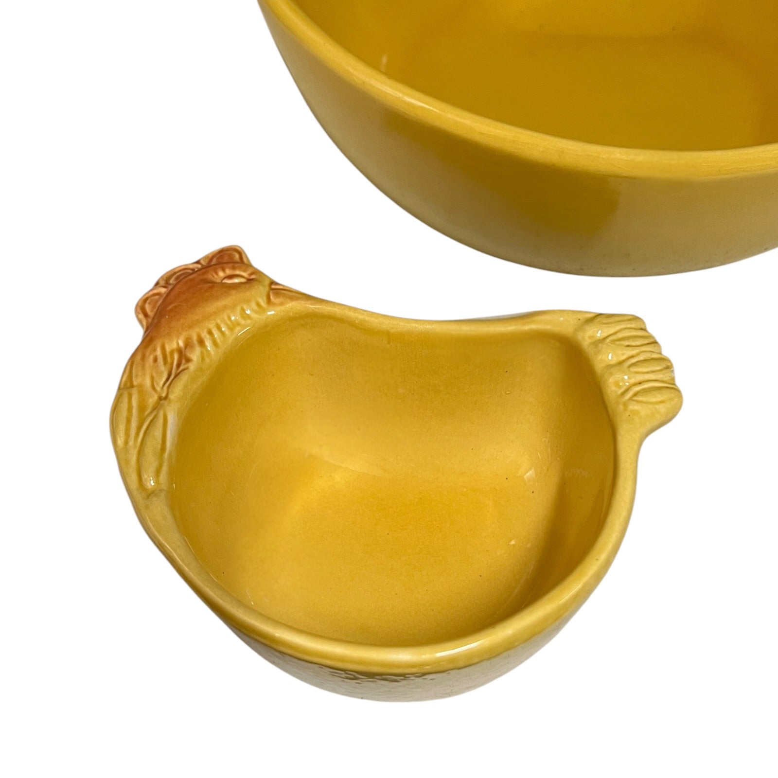 A yellow ceramic chicken-shaped bowl with a textured beak and tail, shown on a white background with another matching bowl partially visible in the upper right.